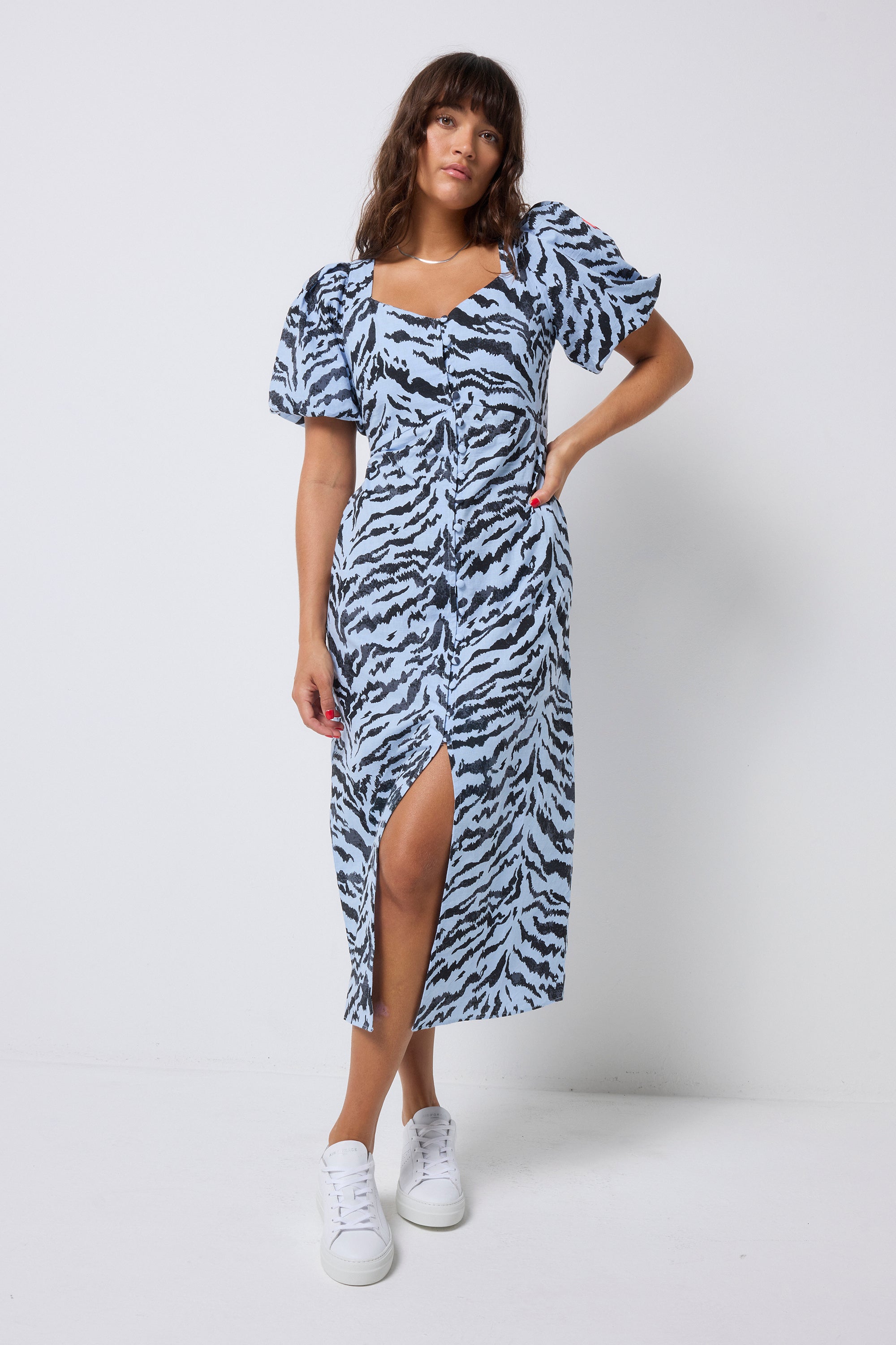 Scamp and Dude Pale Blue With Grey Texture Tiger Puff Sleeve Midi Tea Dress | Model with long dark hair wearing a pale blue midi dress with grey textured tiger print. Worn with white trainers.