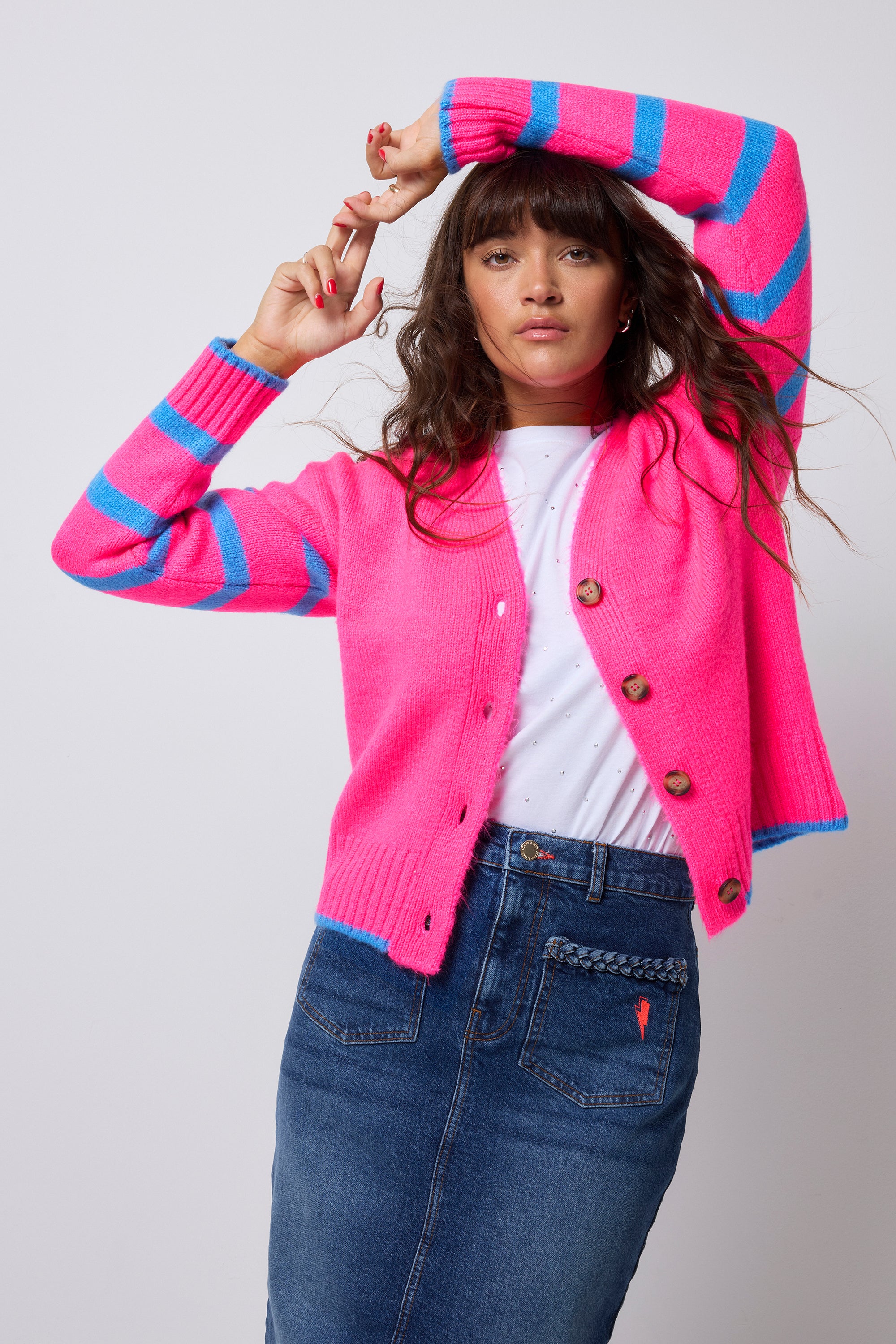 Scamp and Dude Neon Pink with Blue Stripe Cardigan | Model wearing a neon pink cardigan with a blue stripe and piping detail. Worn with a white t-shirt and a blue denim midi skirt.
