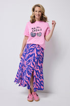 Scamp and Dude Pink Ma Cherie Graphic Print Band T-Shirt | Model wearing a pink graphic t-shirt with ma cherie slogan and cherry applique print. Wone with a pink and blue zebra print skirt and pink trainers.