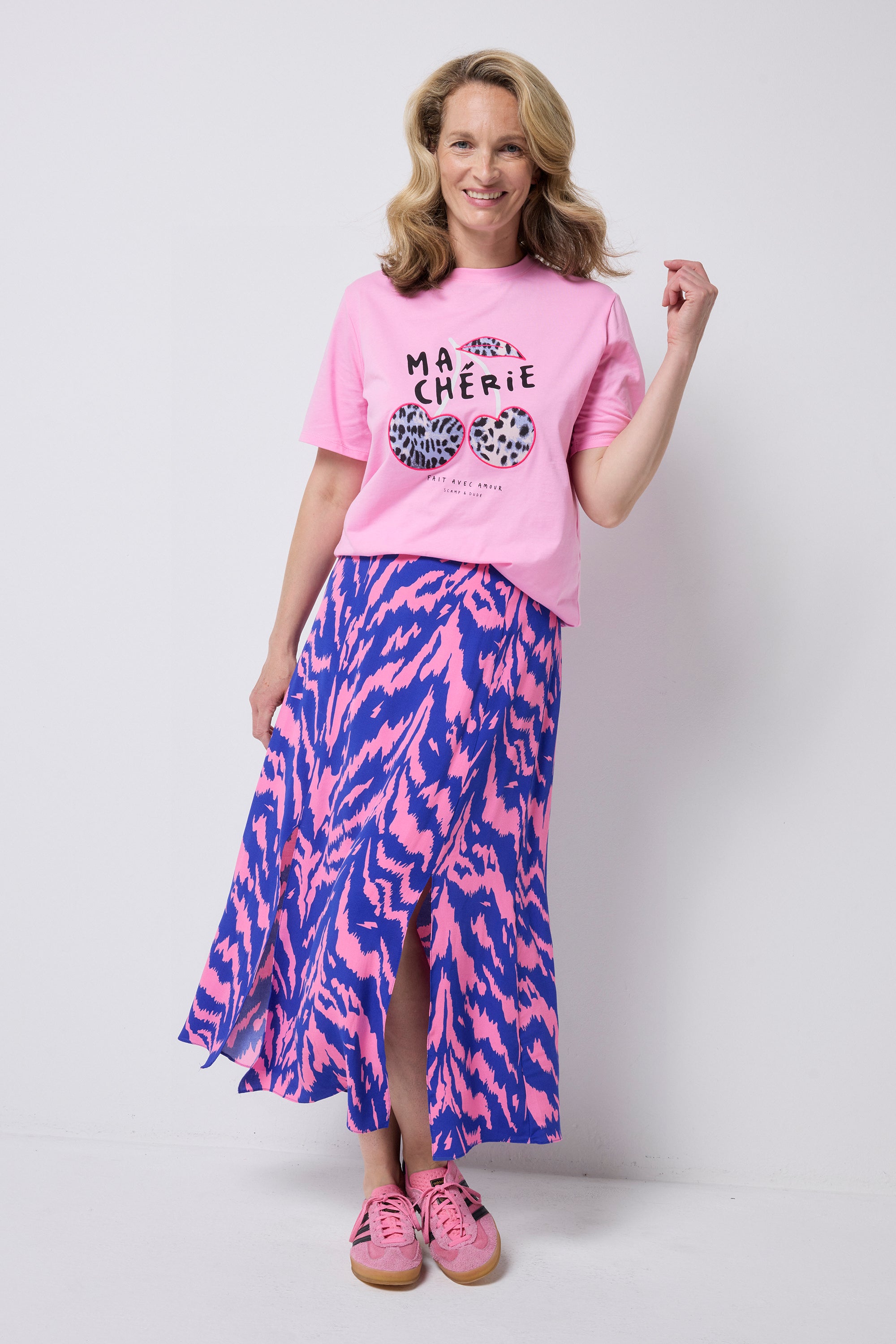 Scamp and Dude Pink Ma Cherie Graphic Print Band T-Shirt | Model wearing a pink graphic t-shirt with ma cherie slogan and cherry applique print. Wone with a pink and blue zebra print skirt and pink trainers.