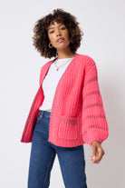 Scamp and Dude Coral with Pink Lurex Stripe Edge to Edge Cardigan | Model wearing a white t-shirt with dark blue jeans and gold jewellery with a coral and pink cardigan.