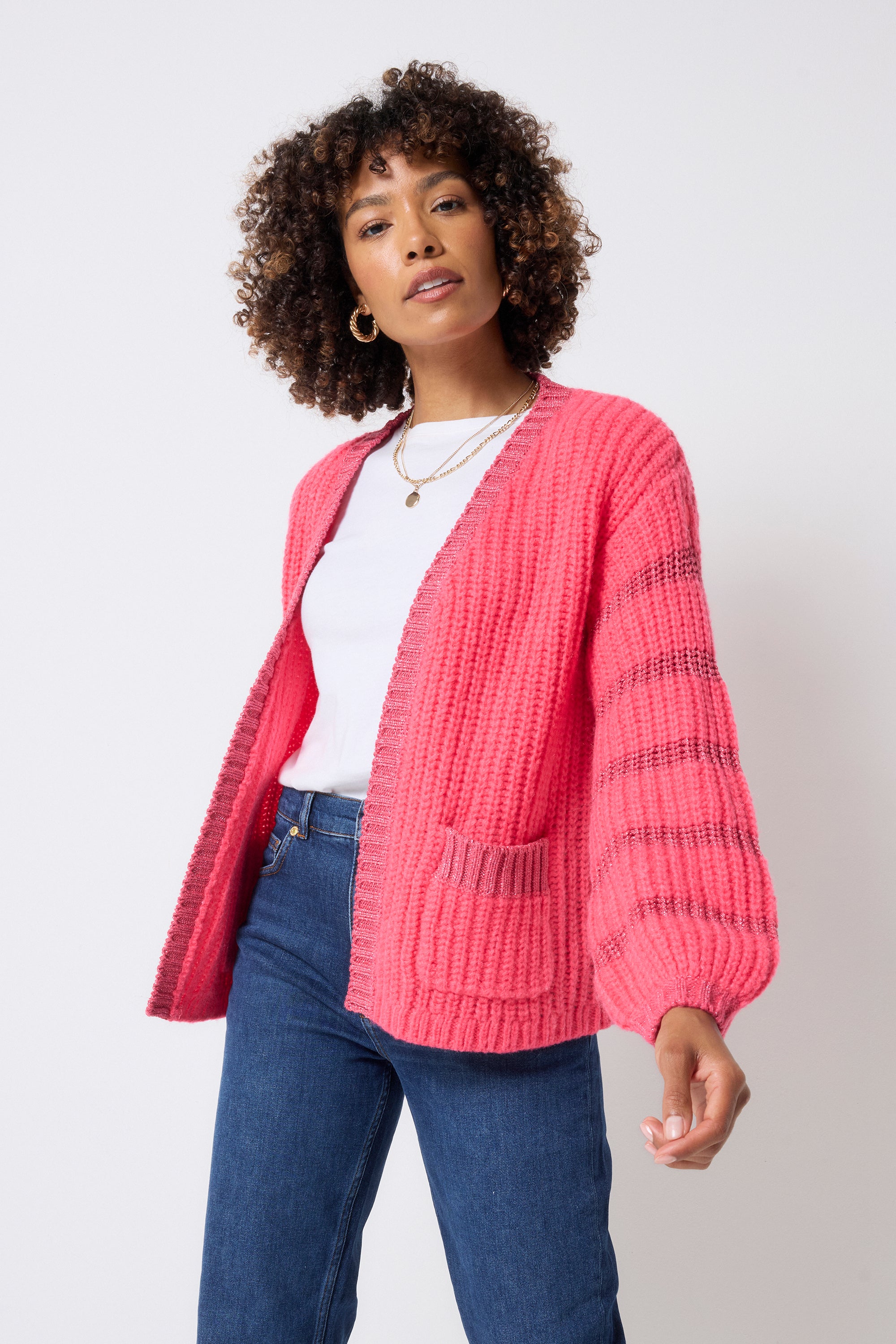 Scamp and Dude Coral with Pink Lurex Stripe Edge to Edge Cardigan | Model wearing a white t-shirt with dark blue jeans and gold jewellery with a coral and pink cardigan.