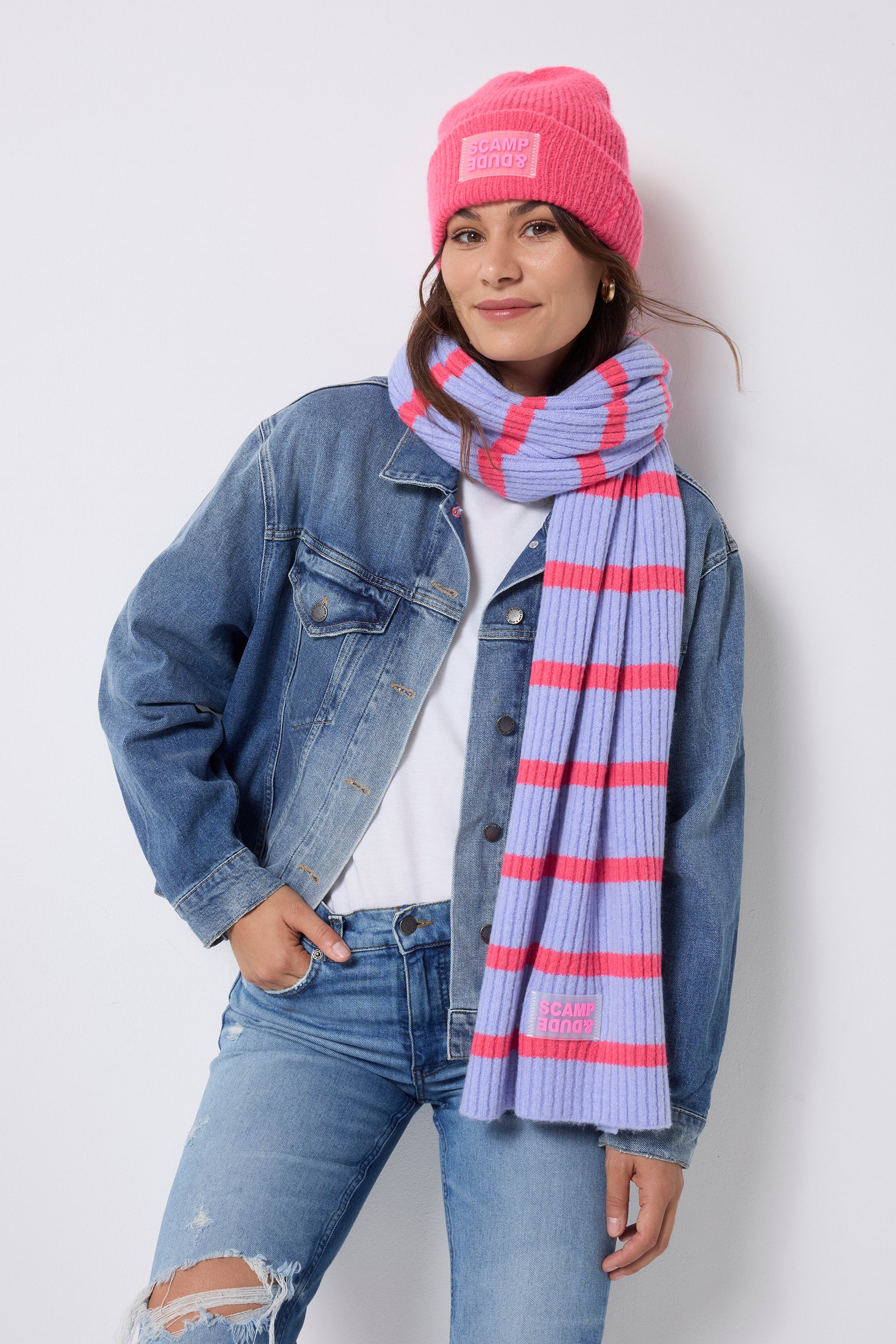 Scamp and Dude Neon Pink and Blue Stripe Ribbed Scarf | Model wearing a pair of distressed jeans with a white t-shirt and denim jacket. Worn with a neon pink beanie and pink and blue stripe scarf.