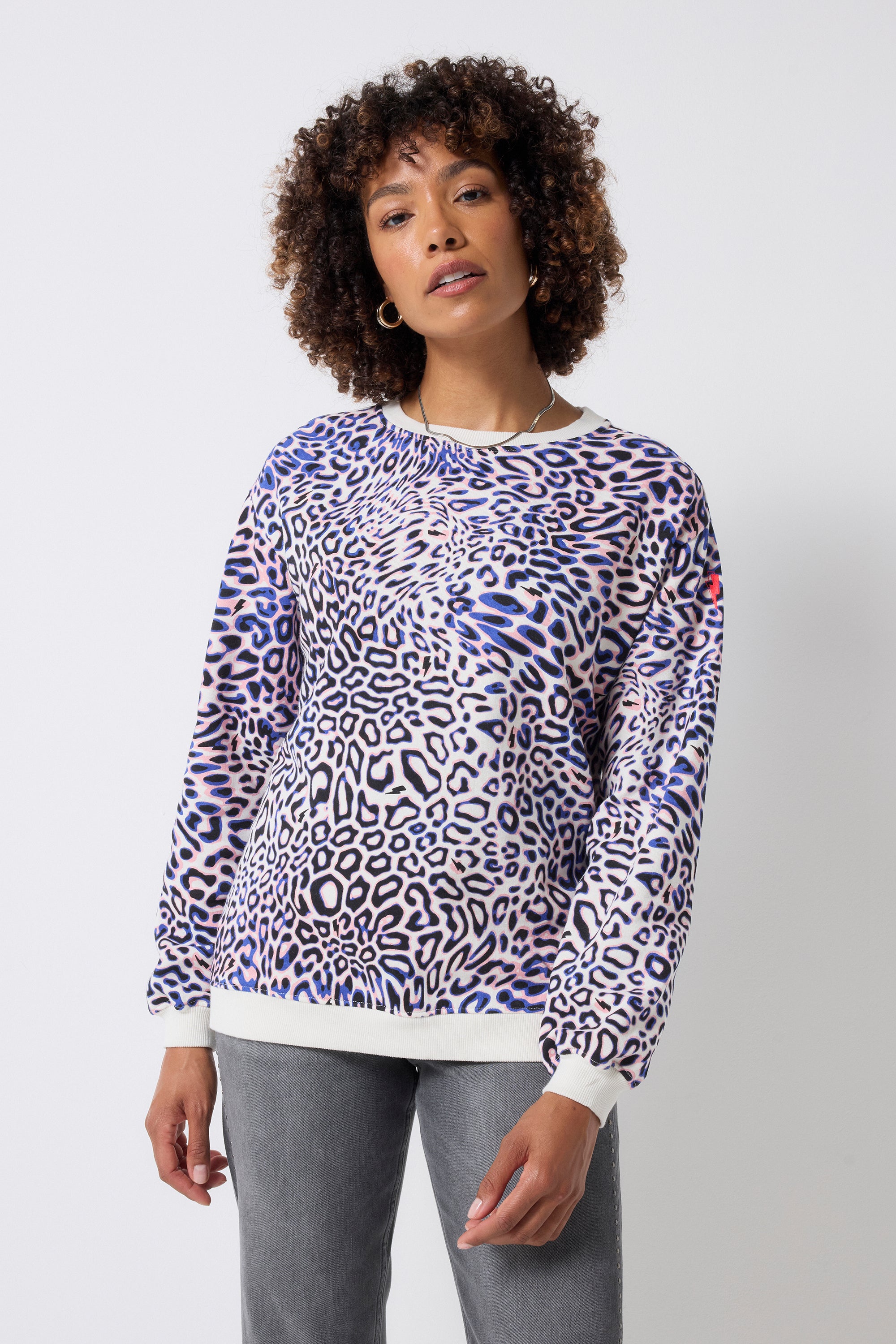 Scamp and Dude Ivory with Blue and Pink Leopard Ray Oversized Sweatshirt | Model wearing a crew neck sweatshirt with blue and pink leopard ray print. Worn with grey studded jeans.