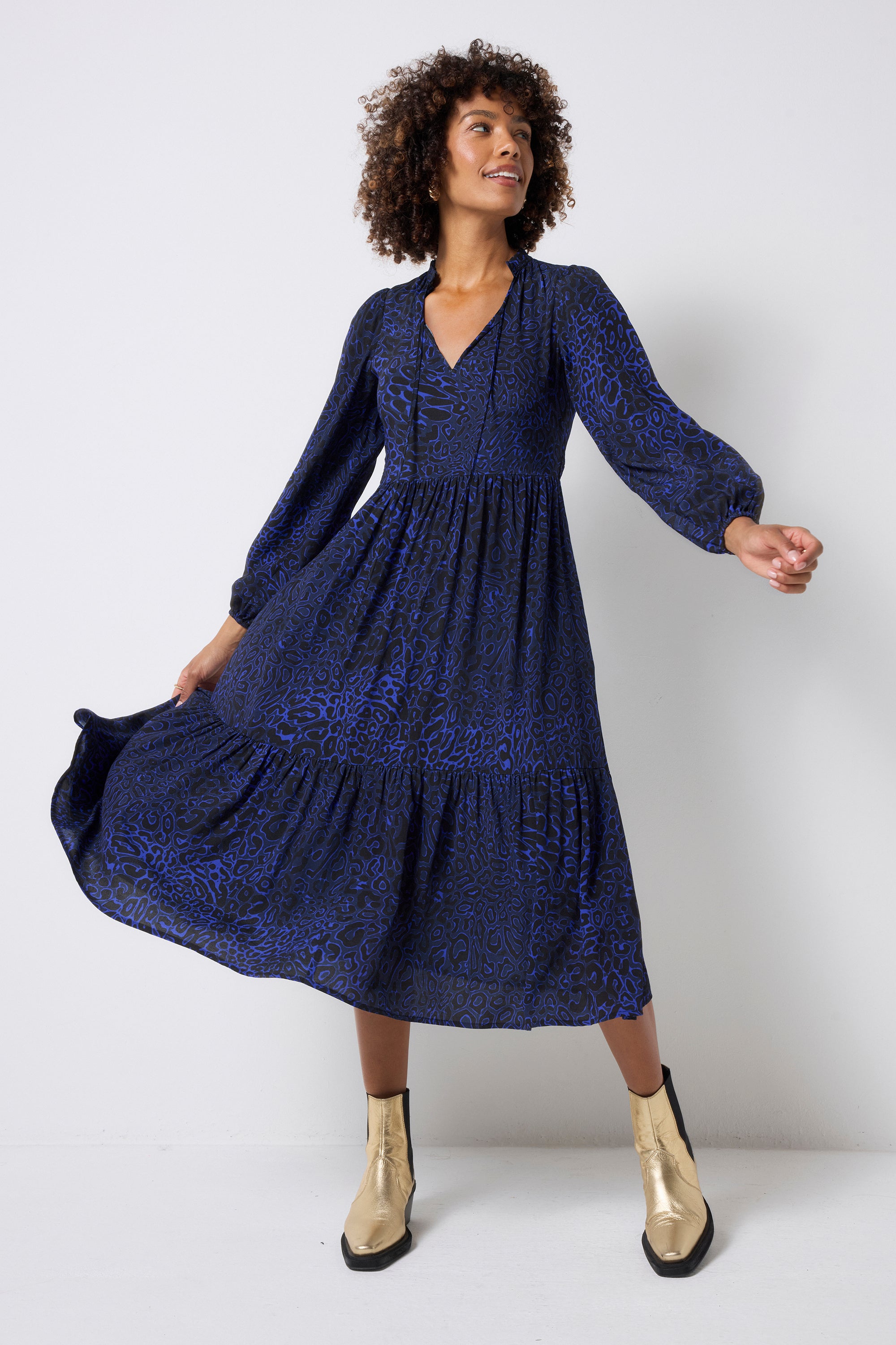 Scamp and Dude Navy Leopard Ray Blouson Sleeve Tie Front Midi Dress | Model wearing a long sleeve navy leopard ray print dress with tie front detail and gold boots.