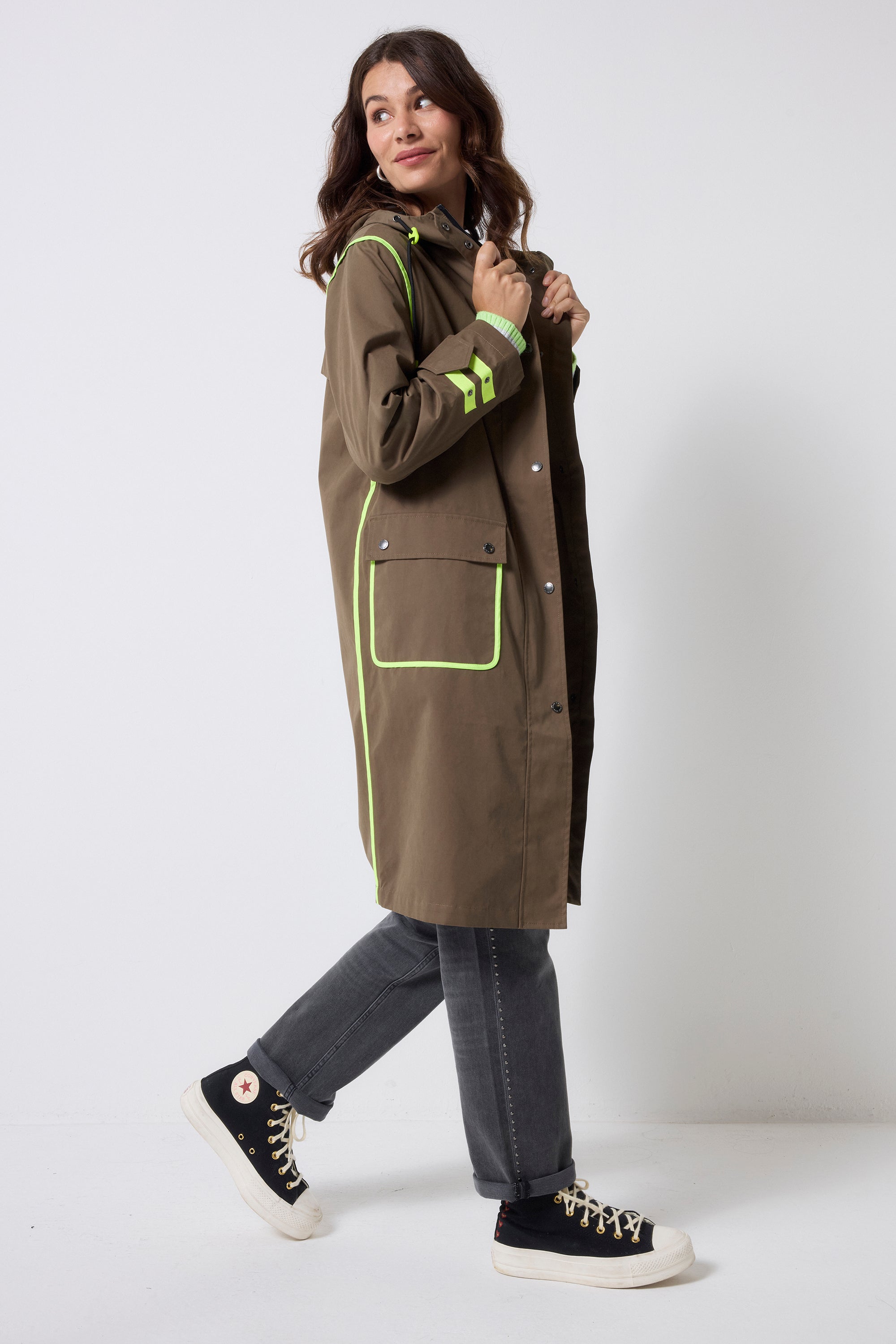 Scamp and Dude Khaki Longer Length Raincoat | Model wearing grey jeans and a khaki raincoat with neon yellow details. Worn with black converse.
