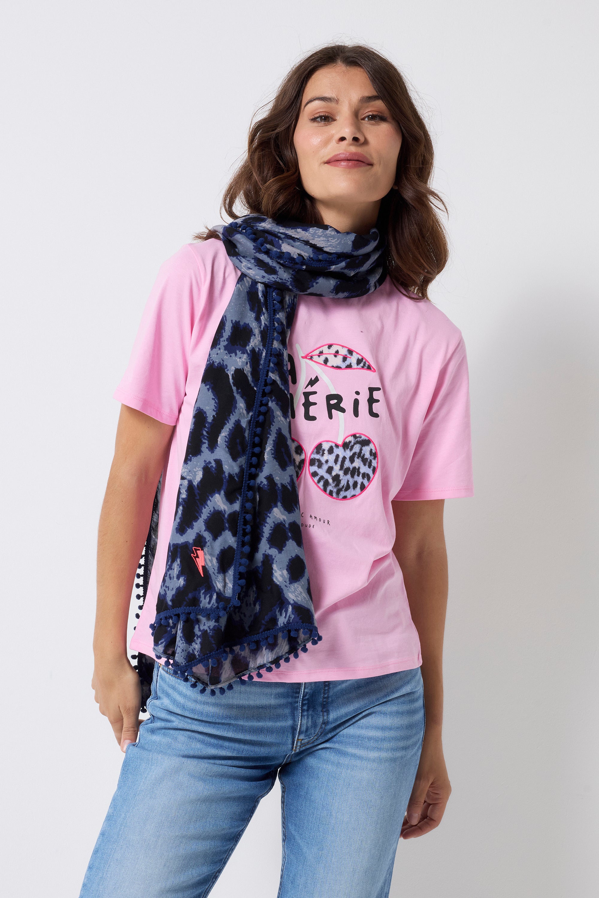 Scamp and Dude Navy Mega Cheetah Super Scarf | Model wearing a pink cherry t-shirt with blue jeans and a navy cheetah super scarf.
