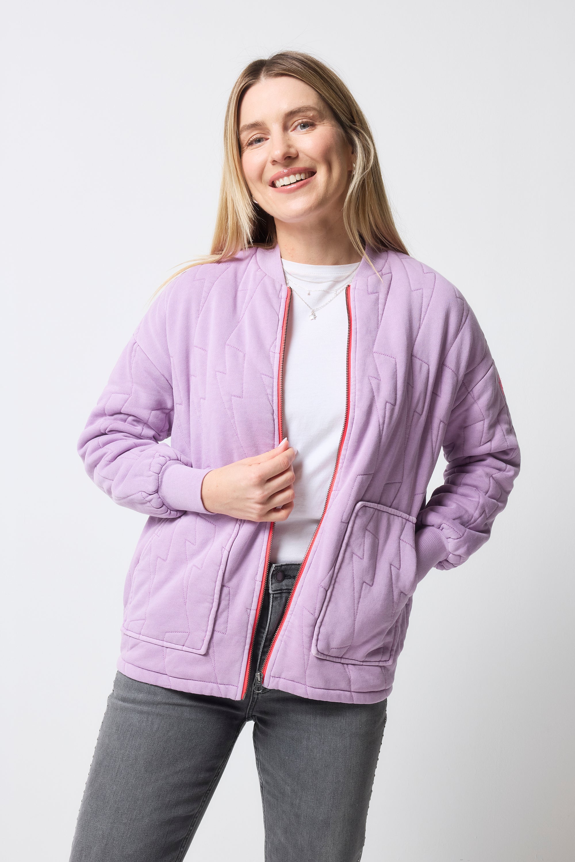 Scamp and Dude Lilac Lightning Bolt Regular Fit Quilted Bomber Jacket | Model wearing a white t-shirt with a pair of grey studded jeans and a lilac bomber jacket.