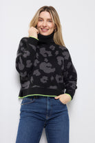 Scamp and Dude Black with Grey Mega Leopard Turtleneck Knitted Jumper | Woman wearing a black leopard knit jumper and blue jeans against a white background.