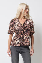 Scamp and Dude Neutral with Black Cheetah Puff Sleeve Button Front Blouse | Model wearing a short sleeve v neck blouse in a neutral cheetah print with black buttons. Worn with grey jeans.