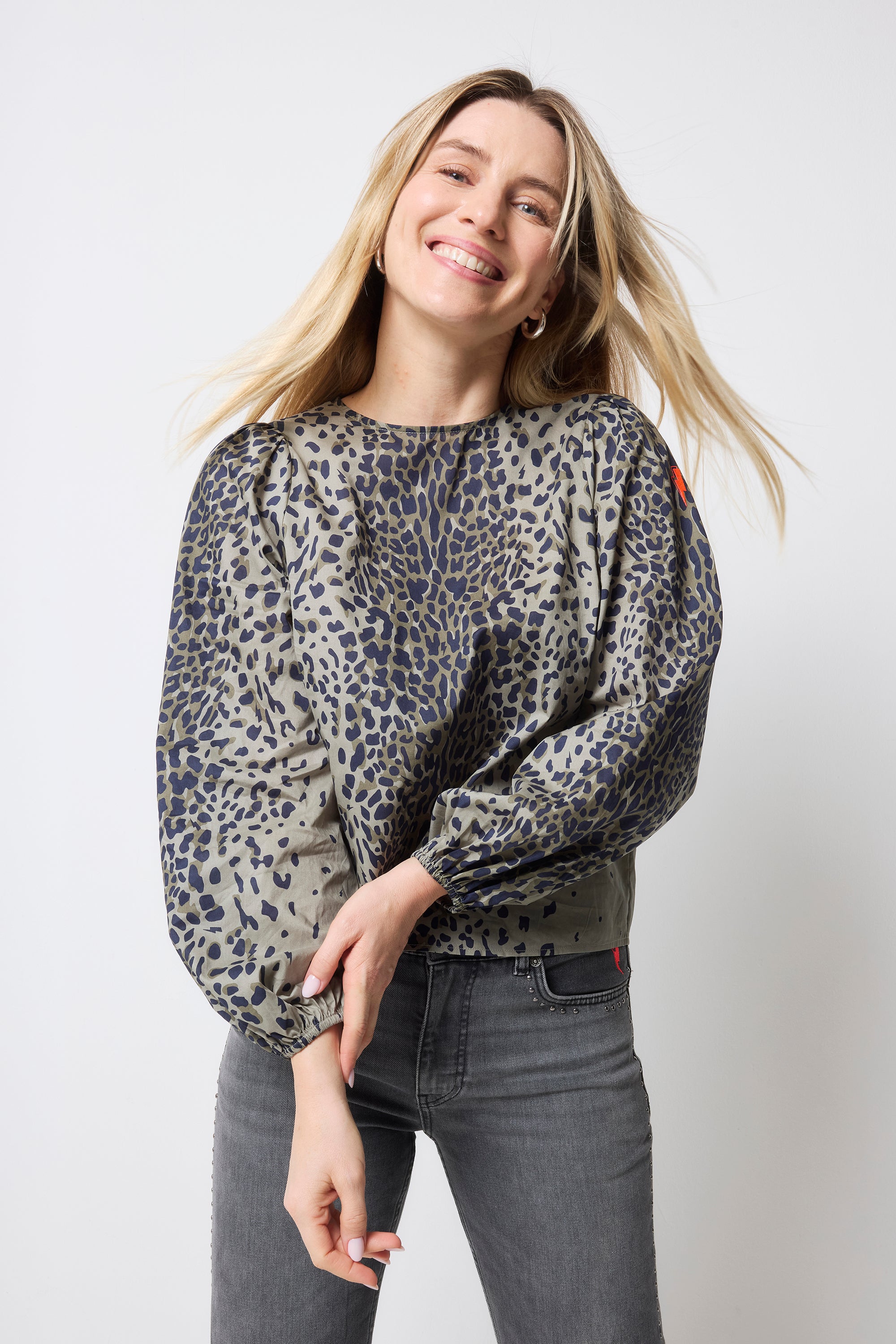 Scamp and Dude Khaki with Black Wild Leopard Blouson Sleeve Top | Model wearing jeans paired with a long sleeve khaki top featuring wild leopard print and bow detail at the back.