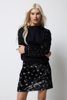Scamp and Dude Black with Black Sequin Sleeve Raglan Sweatshirt | Model wearing a black sweatshirt featuring black sequin sleeves. Paired with a black and silver sequin mini skirt.