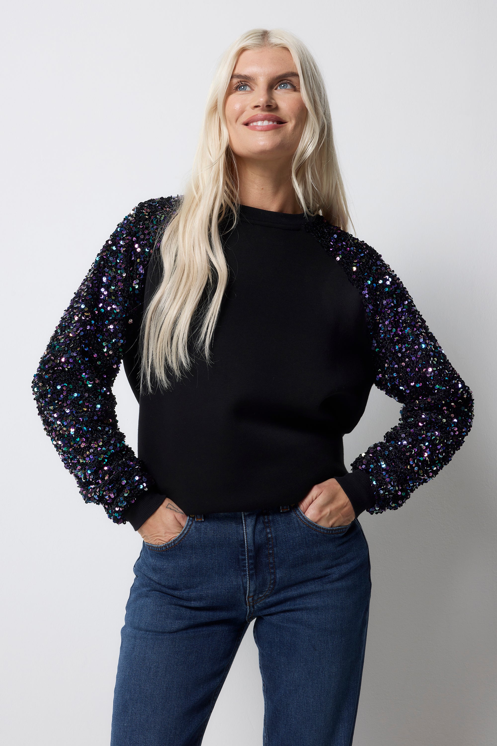 Scamp and Dude Black with Purple Iridescent Sequin Sleeve Raglan Sweatshirt | Model wearing a black sweatshirt with purple iridescent sequins, paired with blue jeans.