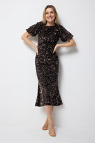Scamp and Dude Bronze Sequin Tie Back Puff Sleeve Velvet Midi Dress | Model wearing a sequin midi dress with puff sleeves and tie back detail paired with strappy gold heels.