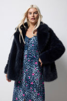 Scamp and Dude Midnight Blue Faux Fur Coat | Model wearing a navy cheetah dress with pink stars. Worn with a midnight blue faux fur coat over the top.