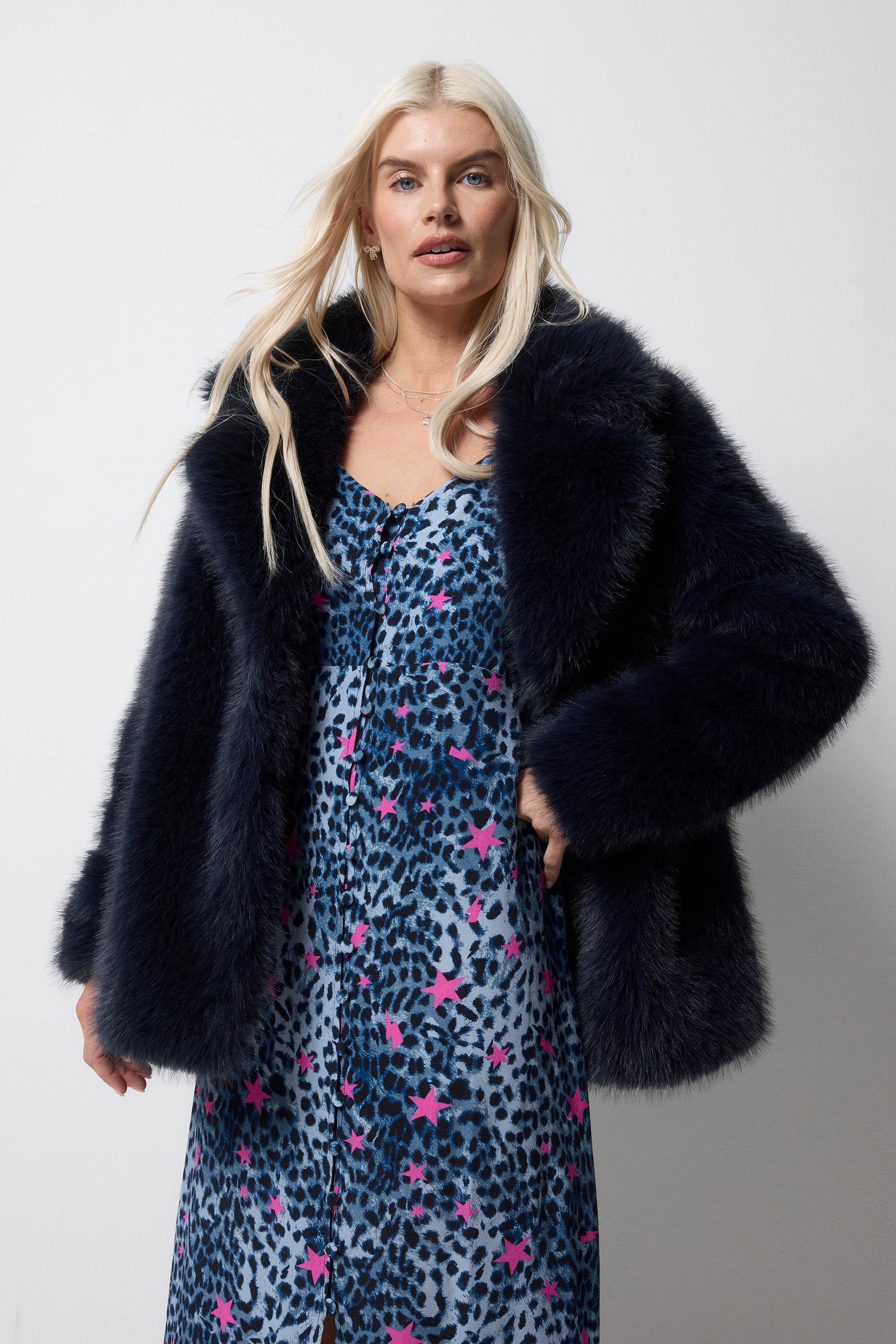 Scamp and Dude Midnight Blue Faux Fur Coat | Model wearing a navy cheetah dress with pink stars. Worn with a midnight blue faux fur coat over the top.