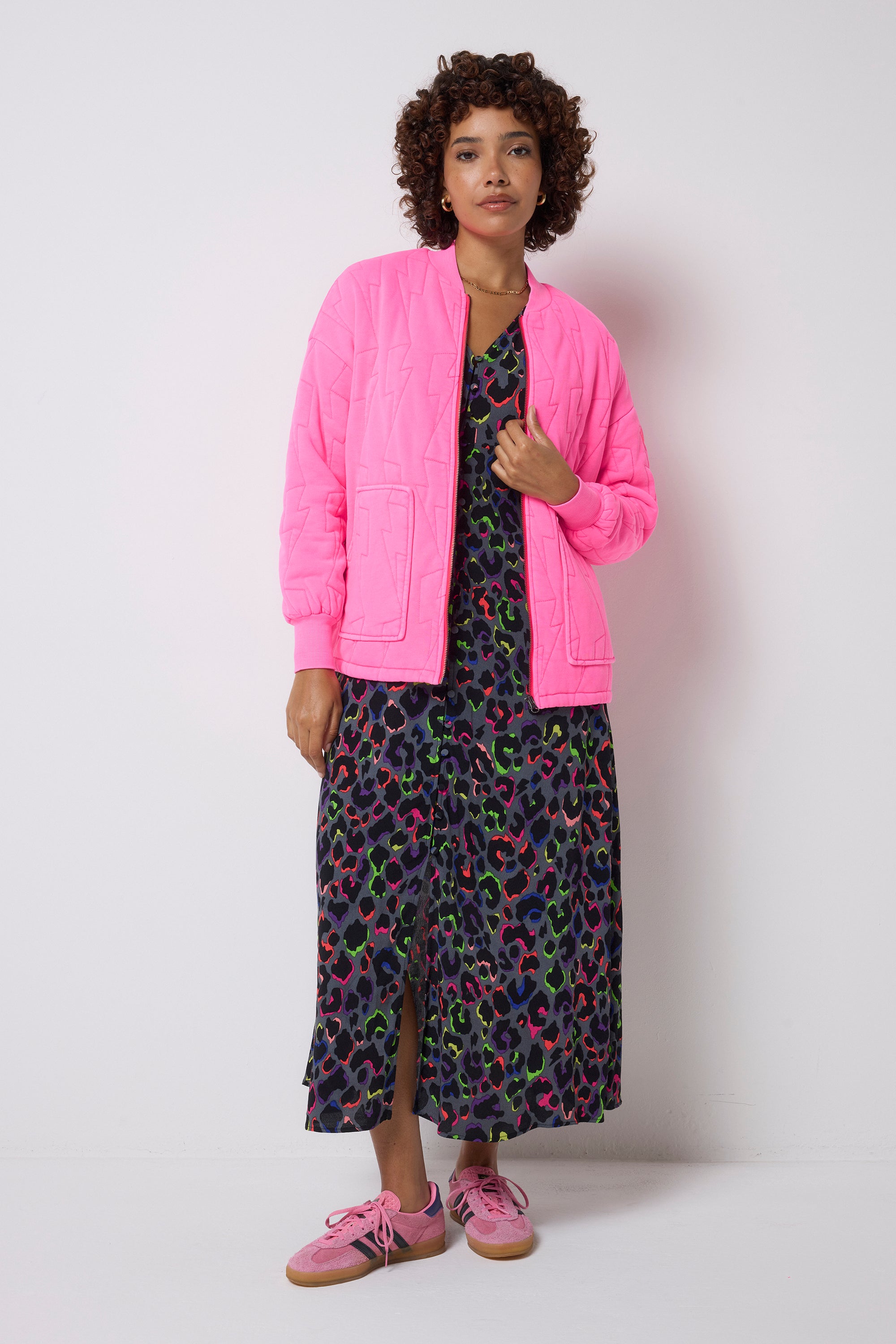 Scamp and Dude Neon Pink Lightning Bolt Regular Fit Quilted Bomber Jacket | Model wearing a pink jacket, grey dress with rainbow leopard print and pink shoes on a white background.