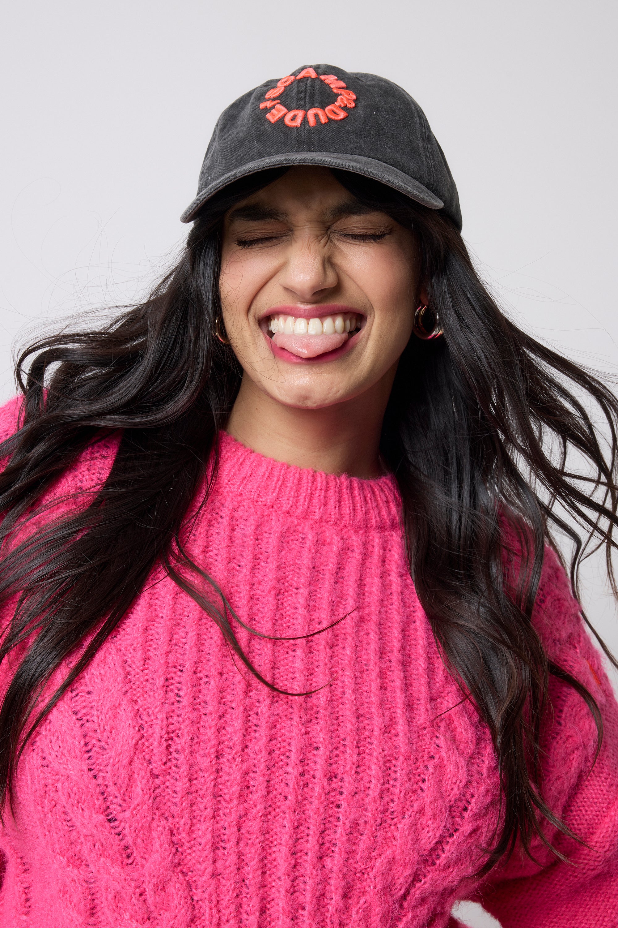 Scamp and Dude Washed Black Graphic Logo Cap | Model wearing a black cap with red text and a pink knit jumper against a white background.