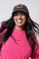 Scamp and Dude Washed Black Graphic Logo Cap | Model wearing a black cap with red text and a pink knit jumper against a white background.