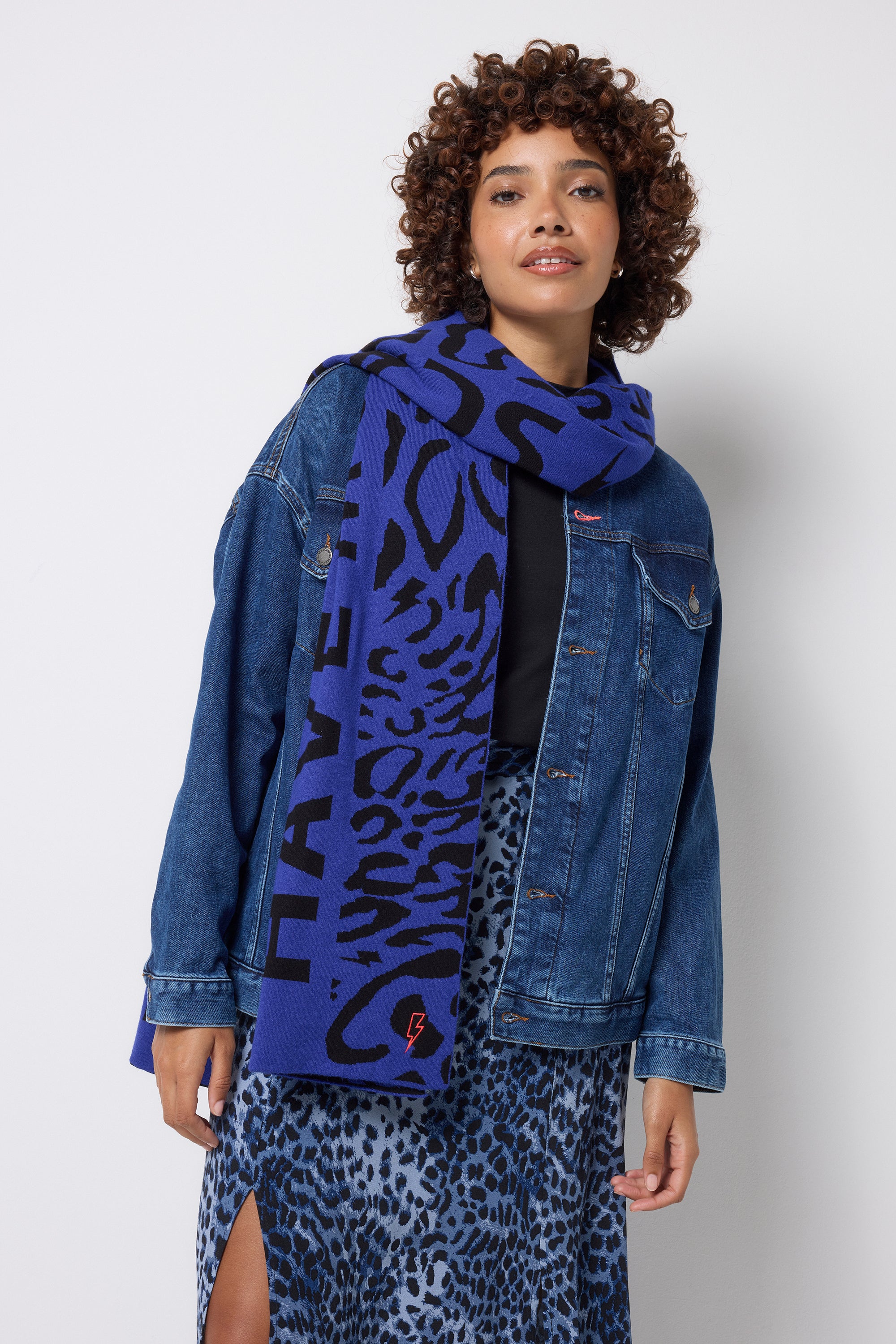 Scamp and Dude Navy with Black Slogan Jacquard Scarf | Model wearing a navy cheetah print skirt, black t-shirt and oversized denim jacket with a blue and black printed scarf. 