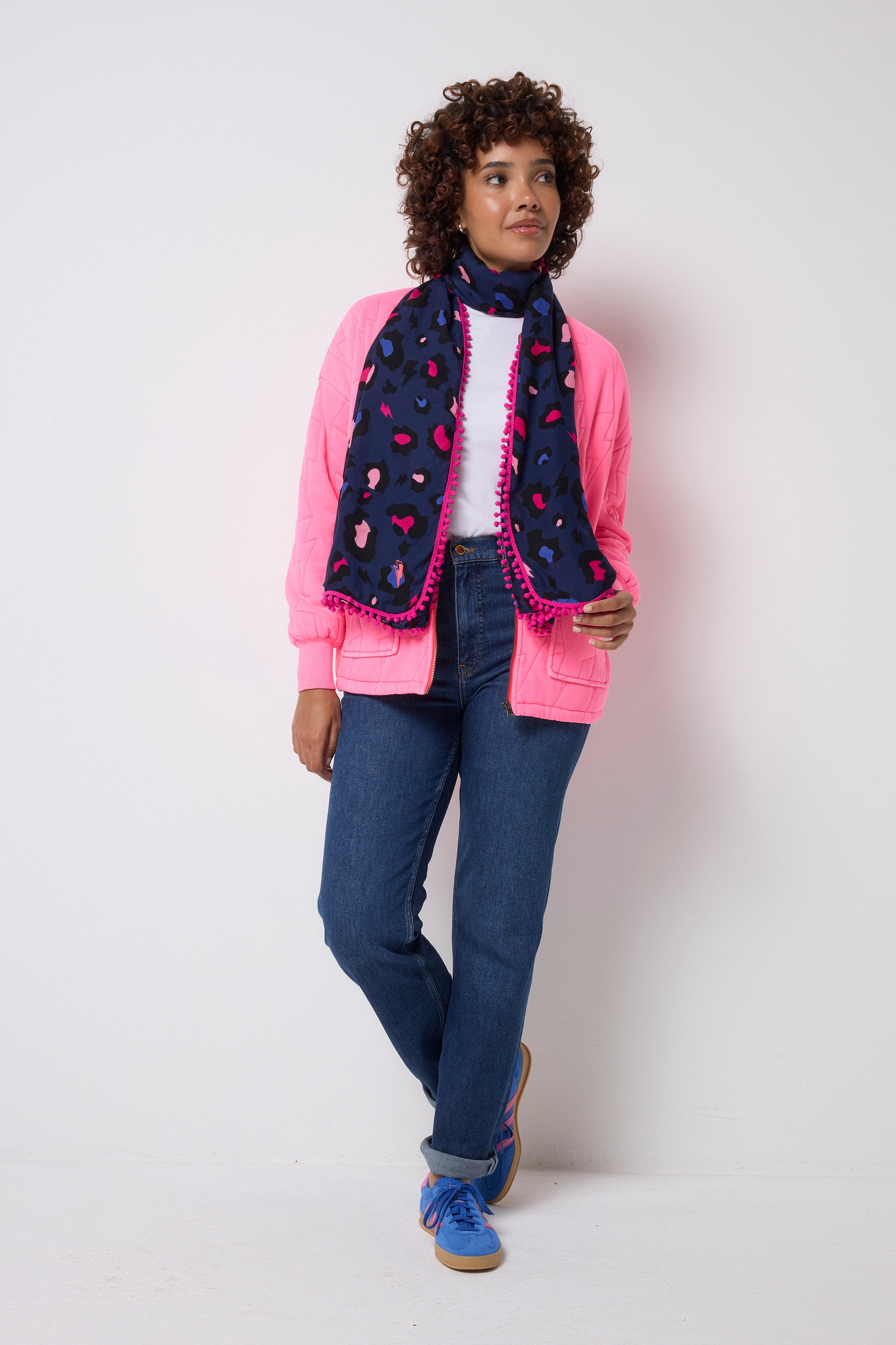 Scamp and Dude Navy with Pink Snow Leopard Charity Super Scarf | Model wearing a navy snow leopard print super scarf with a pink trim. Worn with pair of dark blue jeans, a white t-shirt and pink bomber jacket.