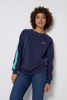 Scamp and Dude Navy with Rainbow Colourblock Sweatshirt | Model wearing dark navy jumper with multi coloured colourblock stripes down the side and sleeves. Worn with dark blue jeans.