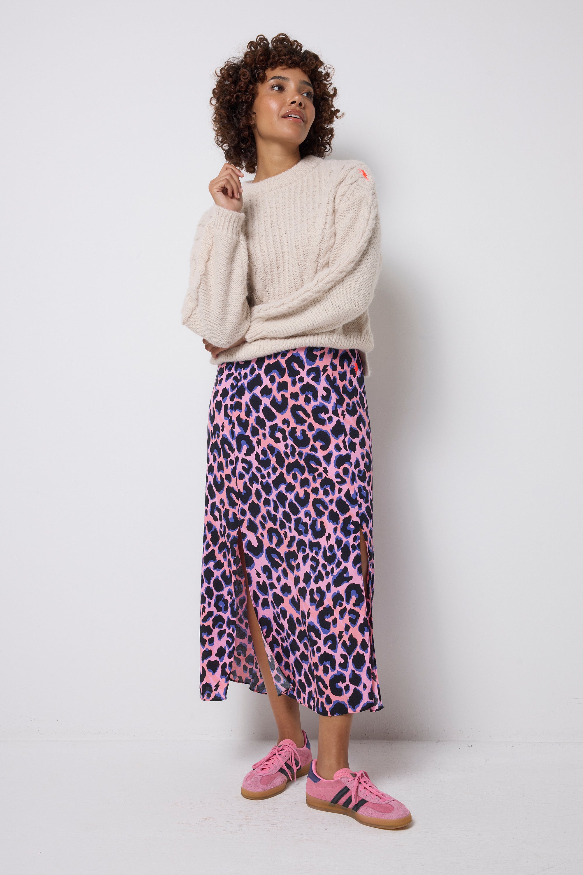 Scamp and Dude Pink with Blue and Black Shadow Leopard Split Front Skirt | Model wearing an oatmeal coloured cable knit jumper with a pink, blue and black leopard print skirt. Worn with pink trainers.