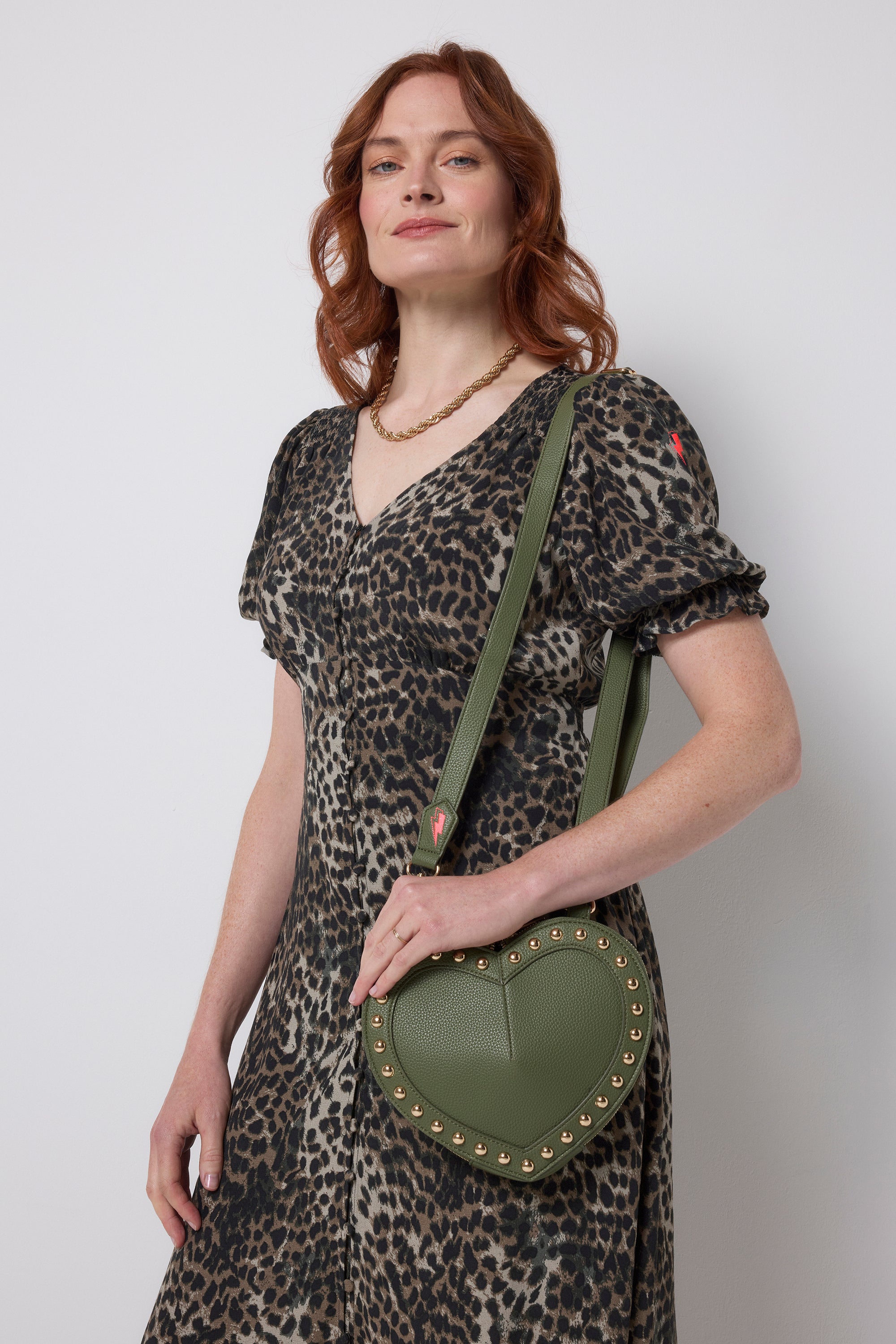 Scamp and Dude Khaki Heart Studded Cross Body Bag | Model wearing a khaki cheetah print dress with a khaki heart shaped bag featuring gold stud detail.