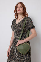 Scamp and Dude Khaki Heart Studded Cross Body Bag | Model wearing a khaki cheetah print dress with a khaki heart shaped bag featuring gold stud detail.