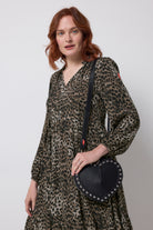 Scamp and Dude Black Heart Studded Cross Body Bag | Model wearing a khaki leopard print long sleeve dress with a black heart shaped bag with silver stud detail.