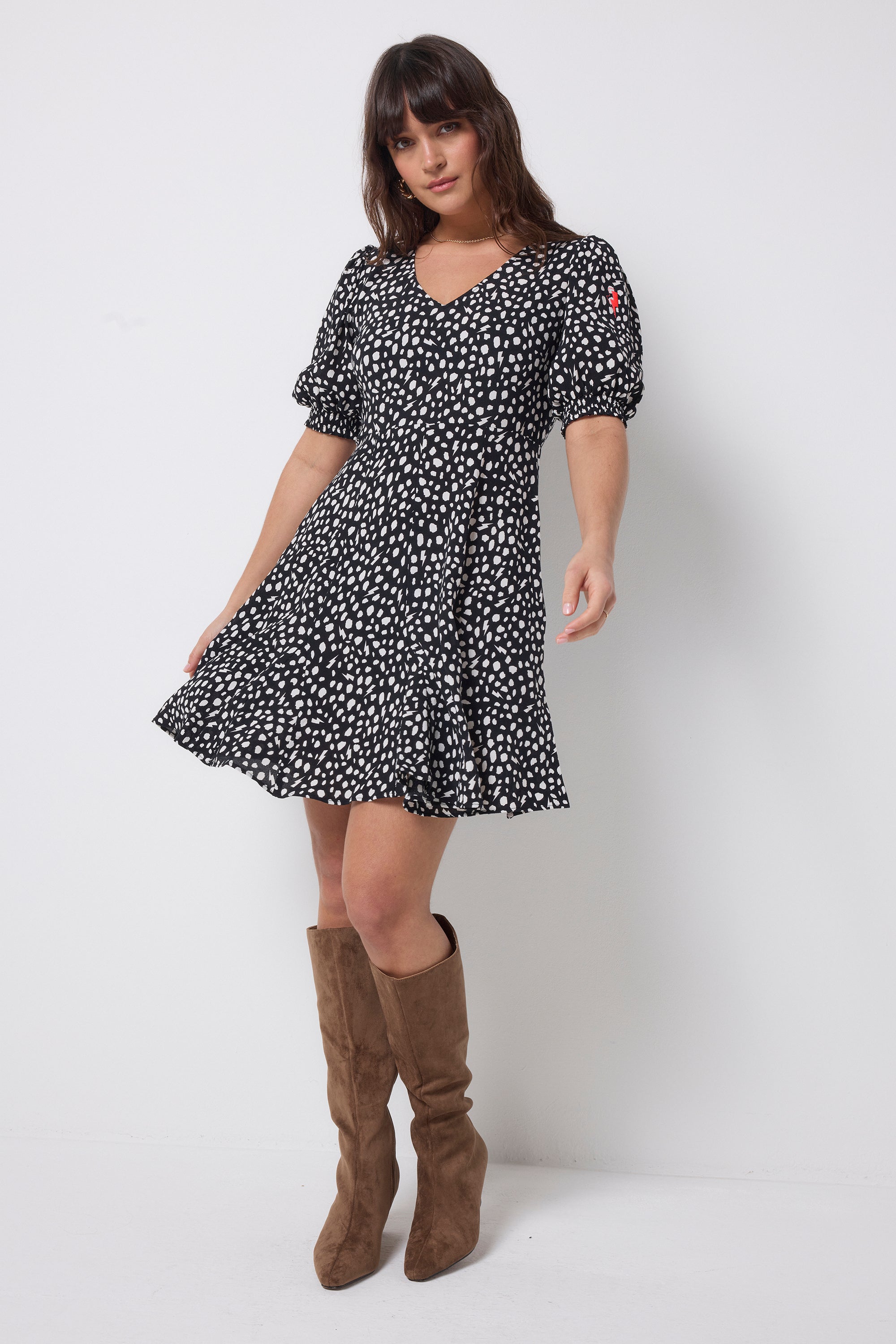 Scamp and Dude Black with White Cheetah Short Skater Dress | Model wearing a black v-neck short skater dress with white cheetah print. Worn with brown suede knee high boots.