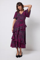 Scamp and Dude Grey with Pink Leopard Ray Ruffle Detail Midi Dress | Model wearing a grey dress with pink leopard ray print and asymmetric ruffle detail. Paired with black bow heels.