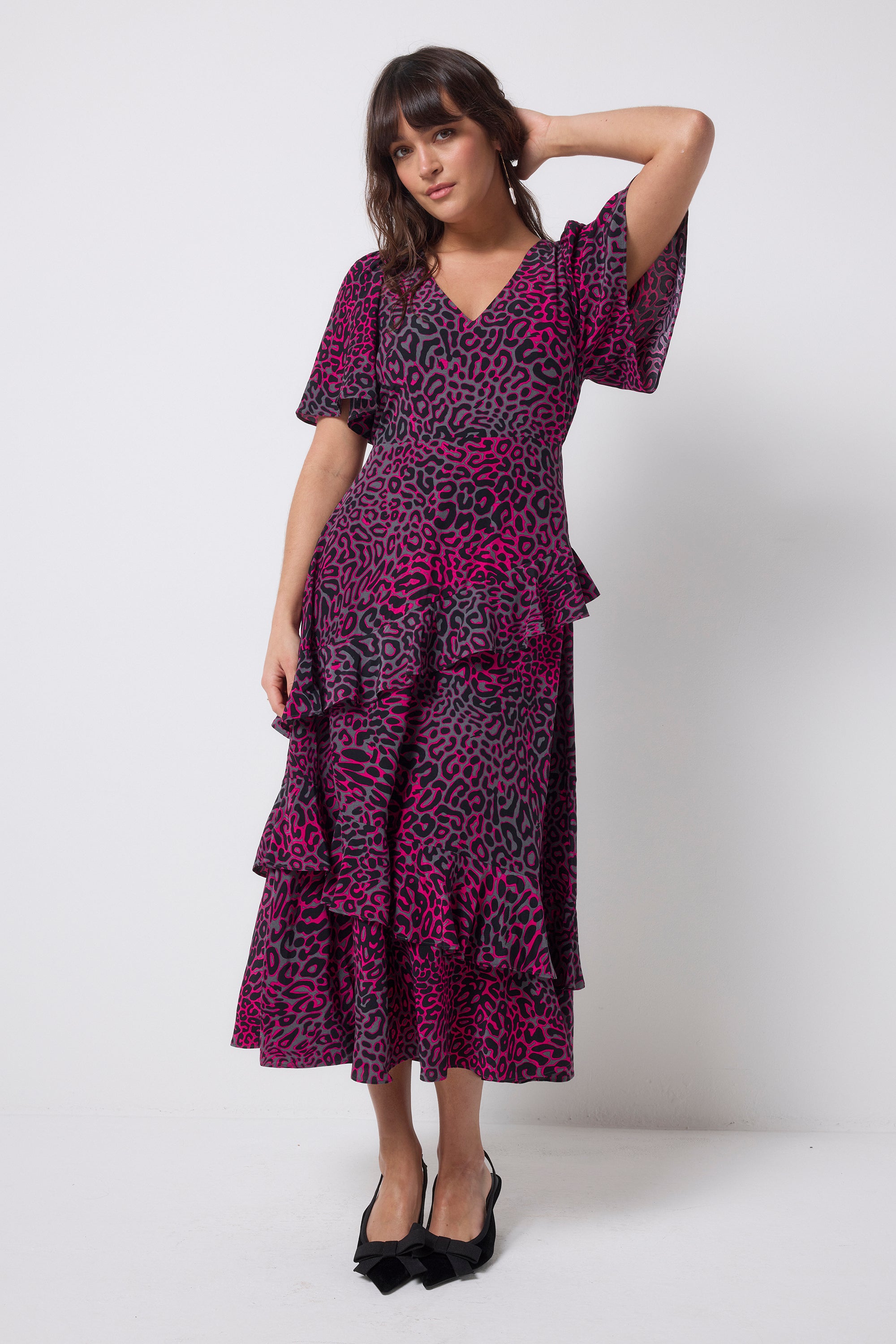 Scamp and Dude Grey with Pink Leopard Ray Ruffle Detail Midi Dress | Model wearing a grey dress with pink leopard ray print and asymmetric ruffle detail. Paired with black bow heels.