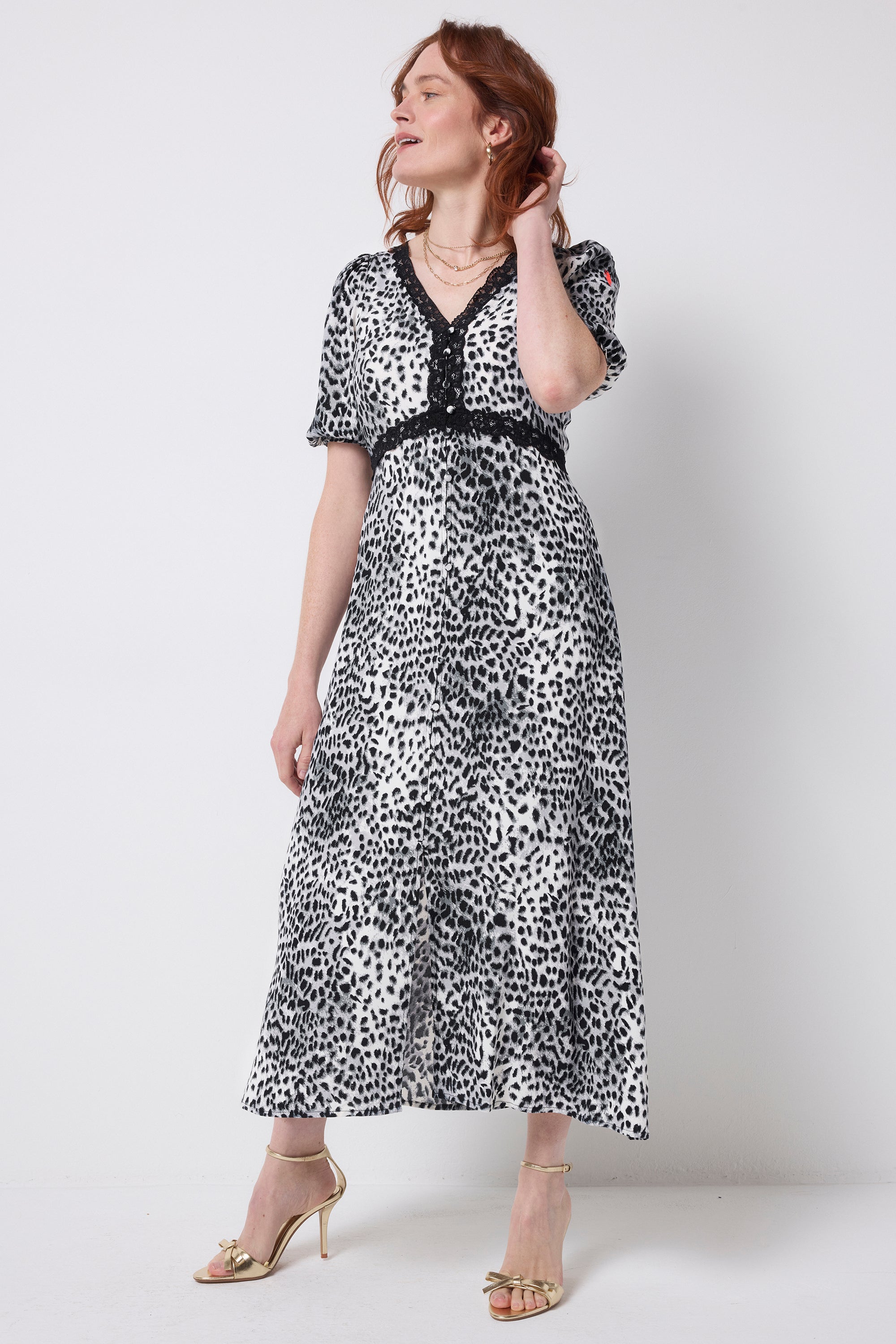 Scamp and Dude Grey Cheetah Lace Trim Puff Sleeve Midi Tea Dress | Model wearing a grey and white cheetah print midi dress with black lace detail. Worn with gold heels.