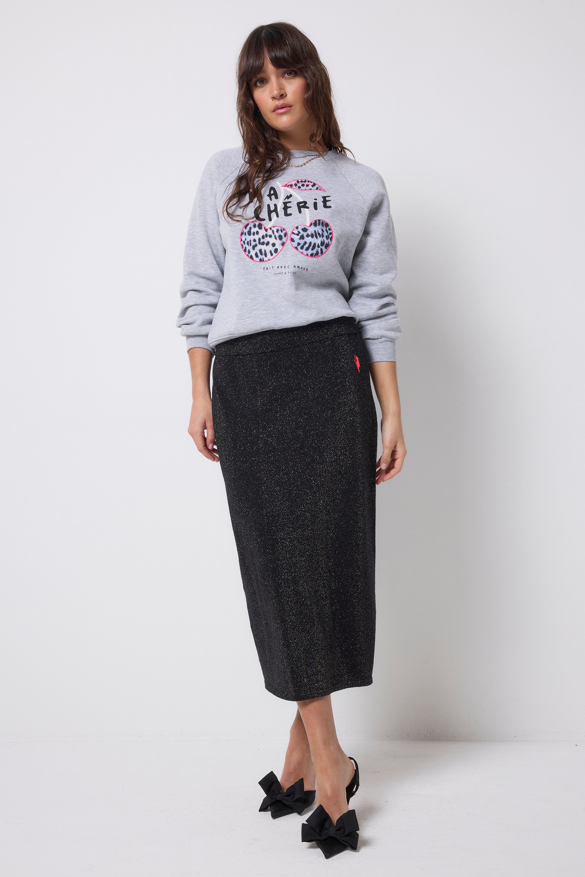 Scamp and Dude Black with Rainbow Lurex Knit Midi Skirt | Model wearing a grey crew neck sweatshirt with a black knitted midi skirt featuring rainbow lurex stripes running through it.