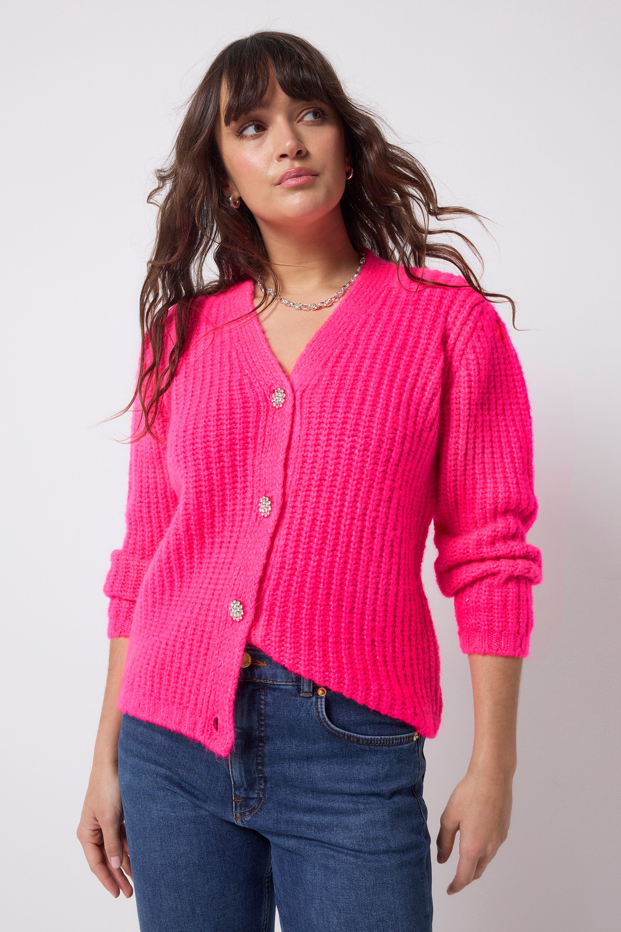 Scamp and Dude Neon Pink Button Through Cardigan | Model wearing a pair of dark blue jeans with a neon pink cardigan that has diamante button detail.