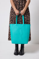 Scamp & Dude Turquoise Lightning Bolt Tote Bag | Model holding a turquoise tote bag with a lightning bolt design, wearing a jaguar print dress and black boots.