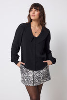 Scamp and Dude Black Collared Blouse | Model wearing a black long sleeve blouse with peter pan collar detail. Worn with a grey cheetah print denim skirt and tights.