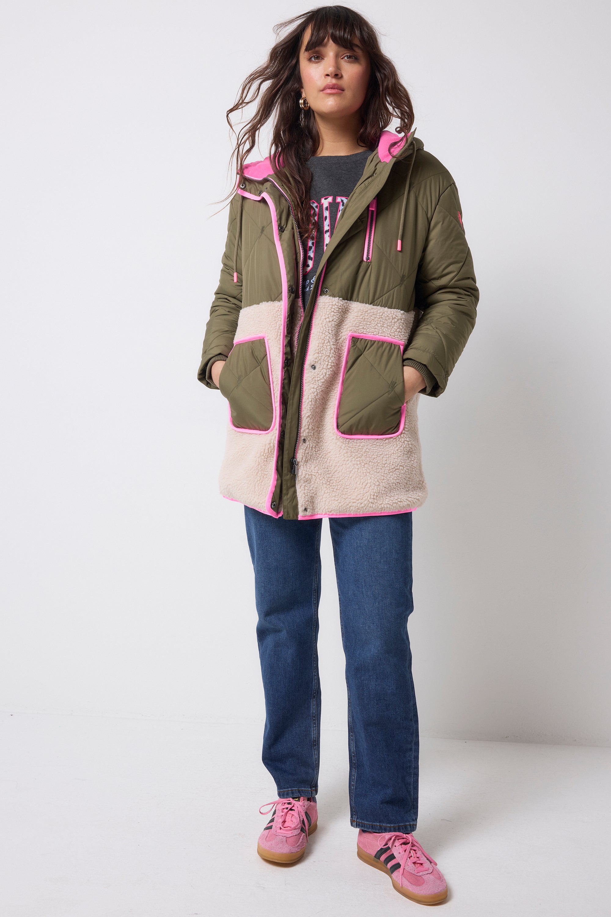 Scamp and Dude Khaki and Pink Quilted Borg Hooded Coat | Model wearing a pair of dark blue jeans with a grey sweatshirt and khaki borg coat which features pink details.