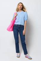 Scamp & Dude Light Blue Short Sleeve Cardigan | Model wearing a light blue short sleeve cardigan with dark blue jeans, colourful shoes and a pink bag.