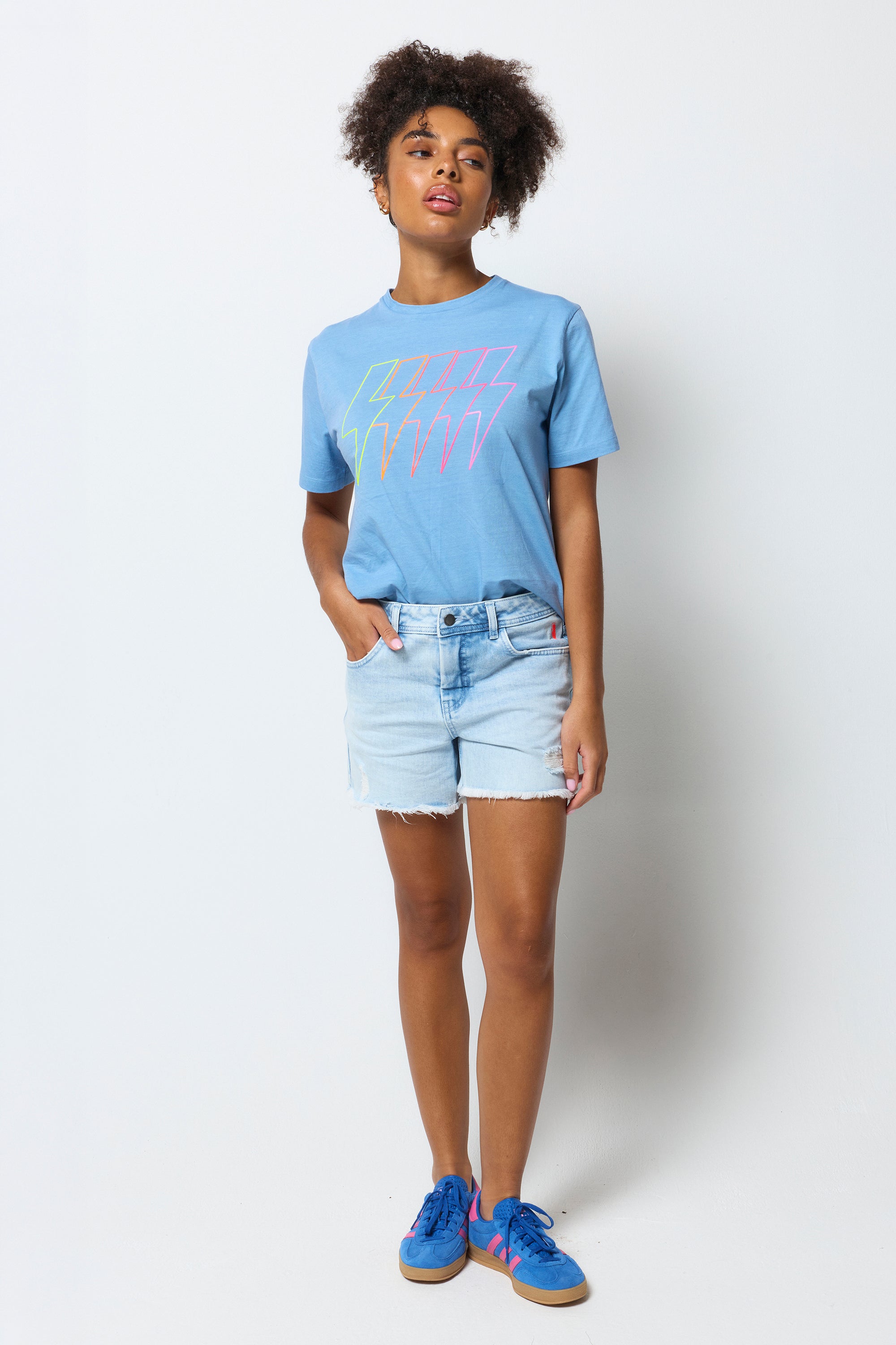 Scamp & Dude Ice Blue Wash Distressed Denim Shorts | Model wearing a light blue graphic t-shirt, denim shorts, and colorful sneakers on a white background.