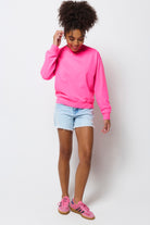 Scamp & Dude | Model wearing a pink sweatshirt, light blue denim shorts, and pink trainers on a white background.