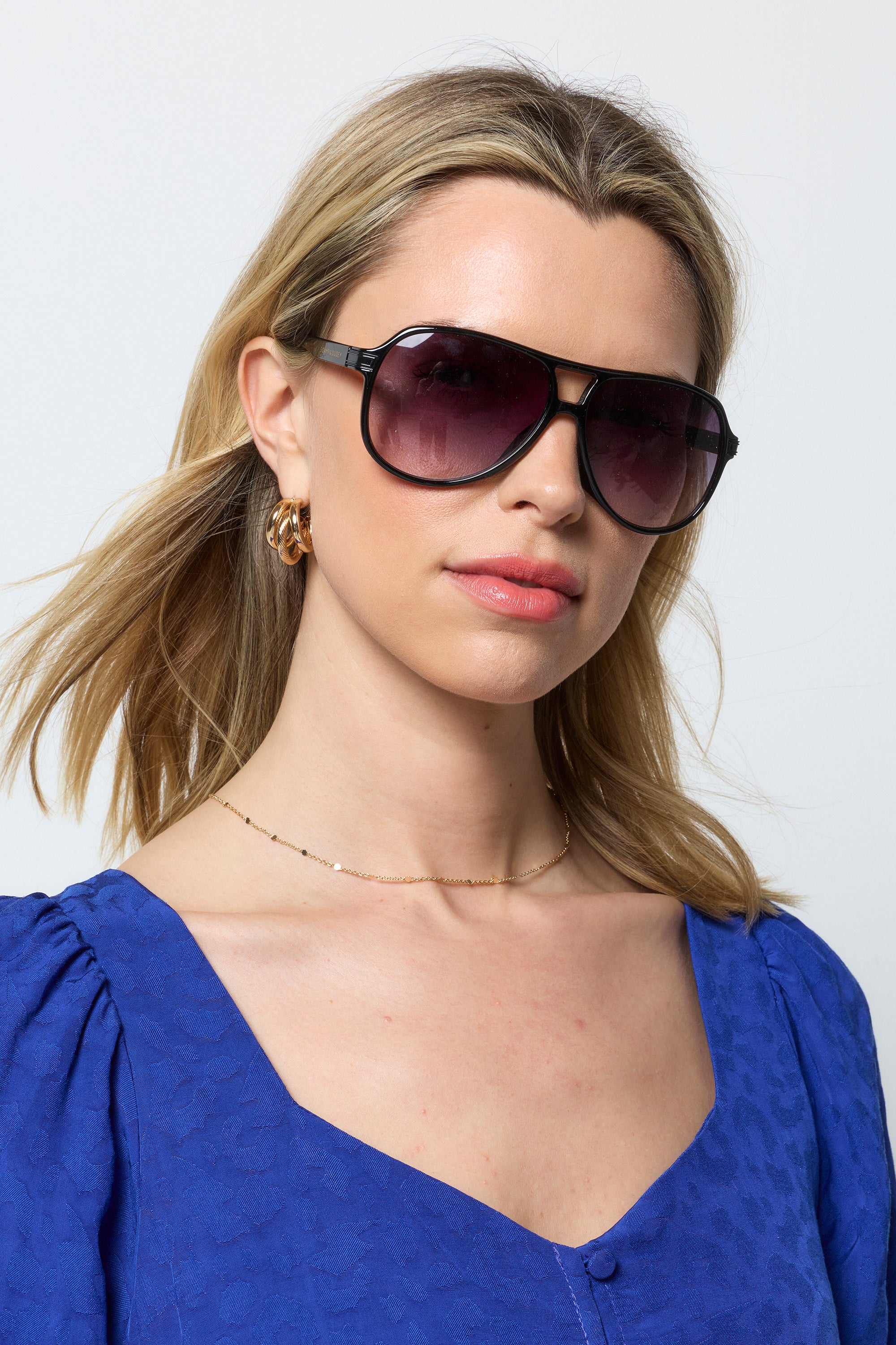 Scamp and Dude Black Aviator Sunglasses | Model wearing a blue broderie dress with gold jewellery and a pair of aviator style sunglasses in a black colour.