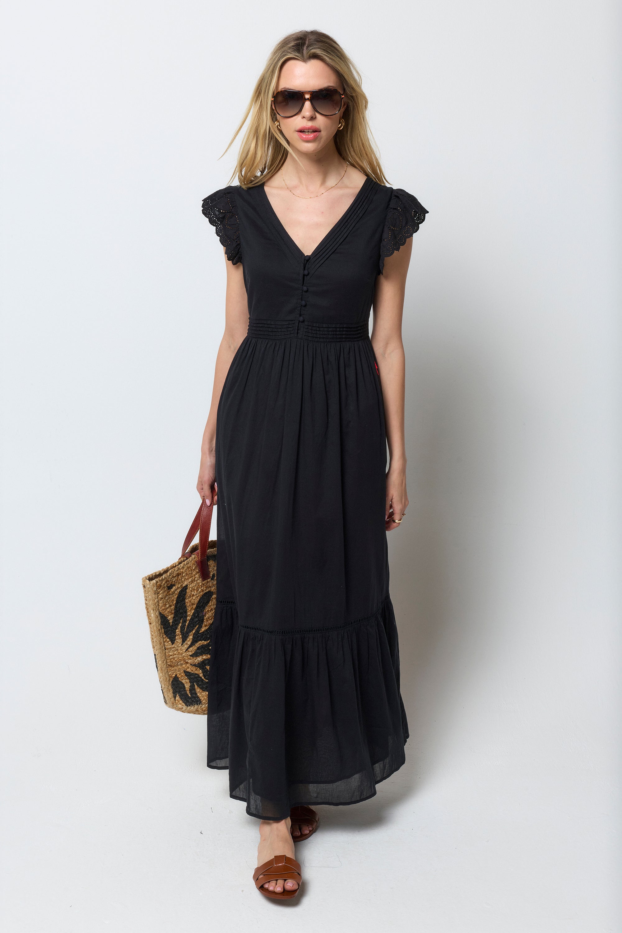 Scamp and Dude Black Broderie Sleeve Pintuck Maxi Dress | Model wearing a black maxi dress with broderie detail. Worn with a straw bag.