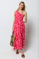 Scamp & Dude Red and Pink Zebra One Shoulder Maxi Dress | Model wear a one should maxi dress in a red and print zebra print. Holding a neutral straw bag with sunstar print.