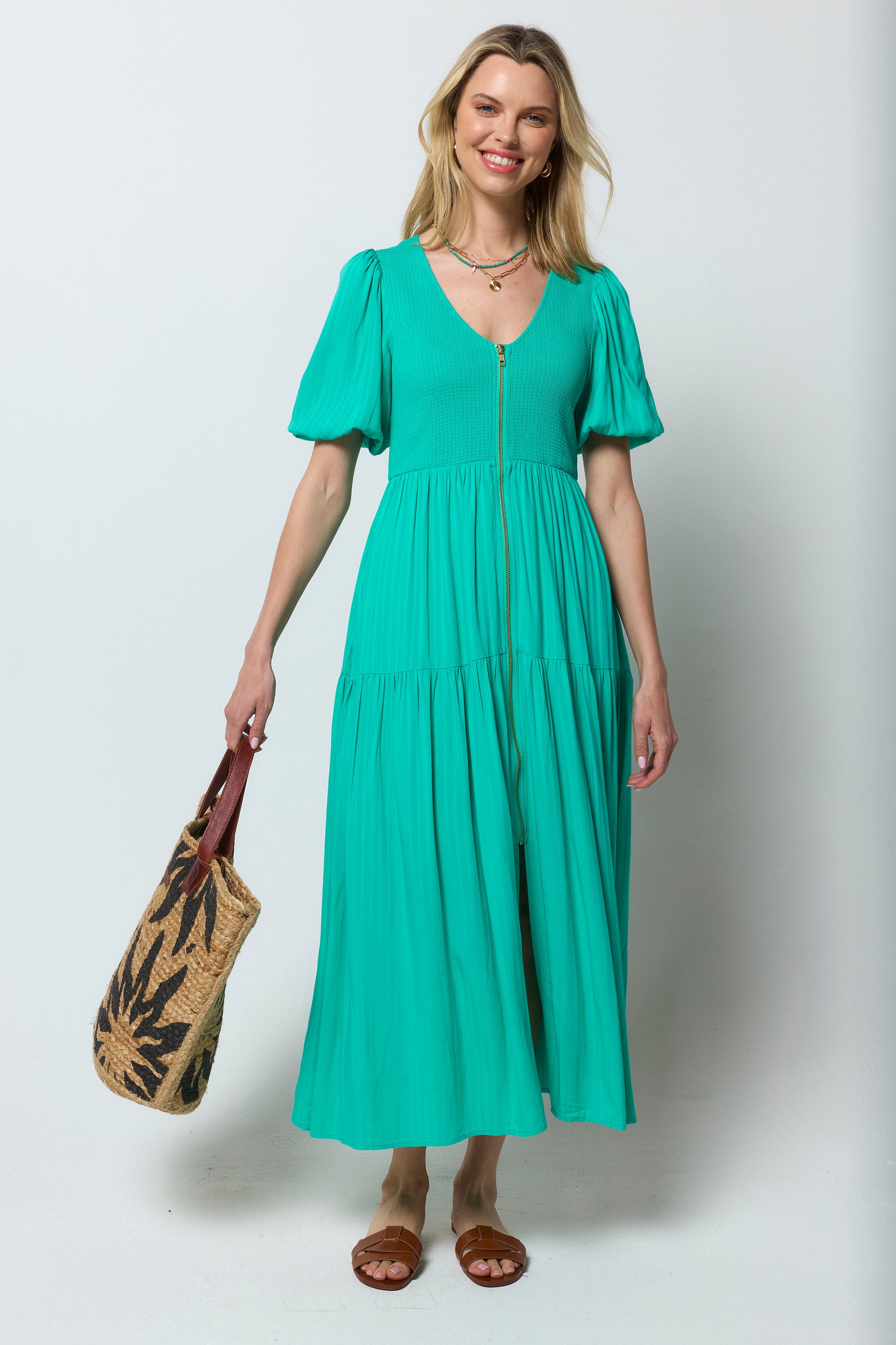Scamp and Dude Green Shirred Zip Detail Midi Dress | Model wearing a green midi dress with shirred detail and zip front. Worn with brown sandals and neutral straw bag.