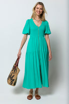Scamp and Dude Green Shirred Zip Detail Midi Dress | Model wearing a green midi dress with shirred detail and zip front. Worn with brown sandals and neutral straw bag.