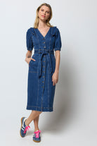 Scamp and Dude Indigo Frill Sleeve Midi Denim Dress | Model wearing a dark blue denim dress with frill detail on the should and a tie waist belt.