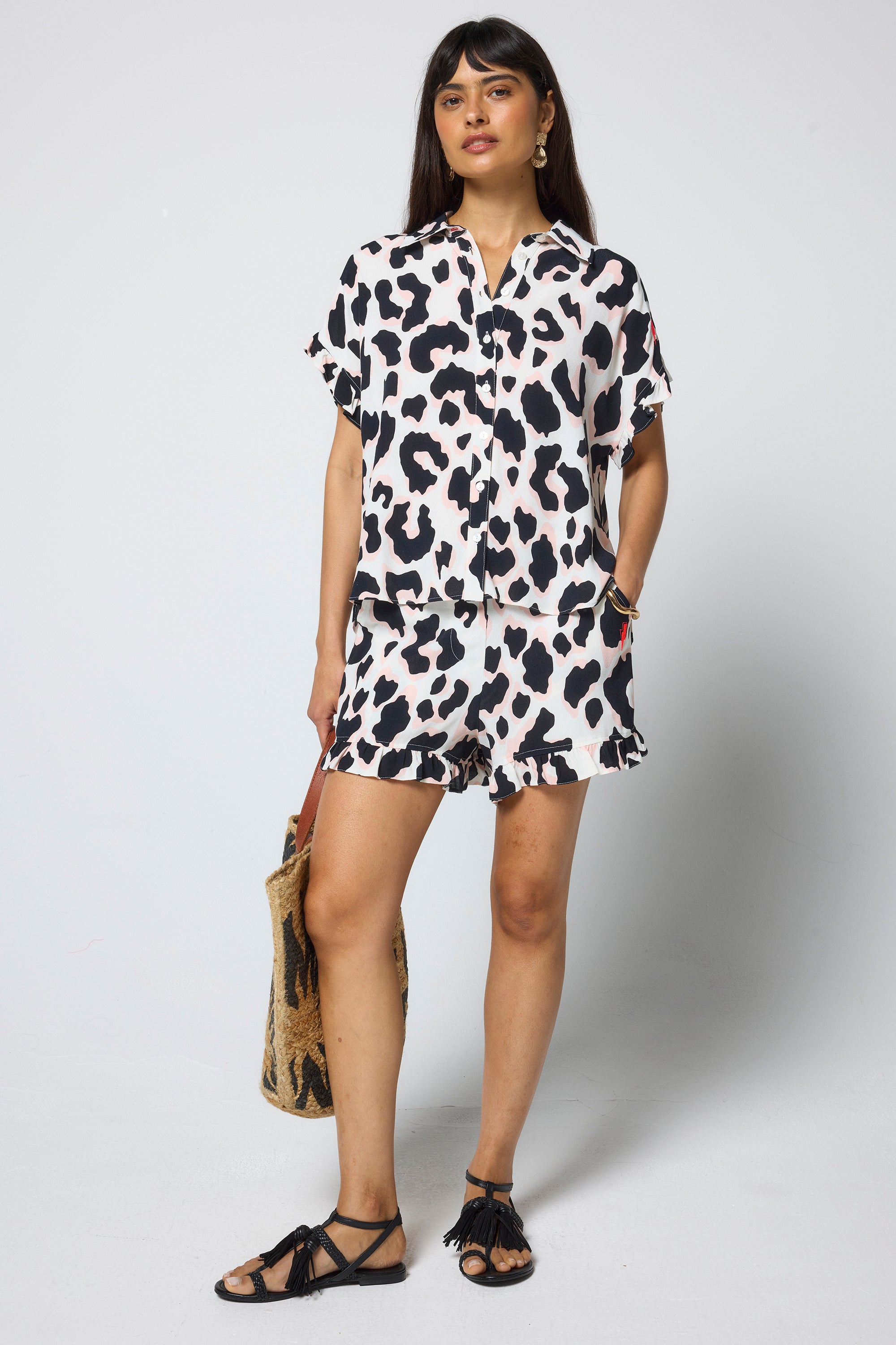 Scamp and Dude Ivory with Neutral and Black Leopard Frill Sleeve Shirt | Model wearing a ivory frill sleeve shirt with leopard print. Worn with matching shorts, black sandals and a straw bag.