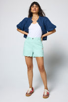 Scamp and Dude Pale Green Scallop Denim Shorts | Model wearing a pair of green denim scallop shorts with a white t shirt and denim shacket.